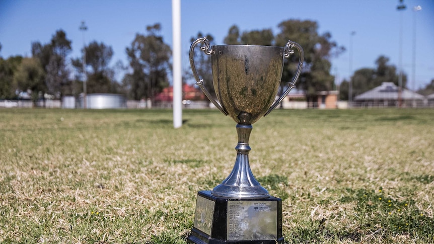 A silver trophy in front of goal posts at a football field.