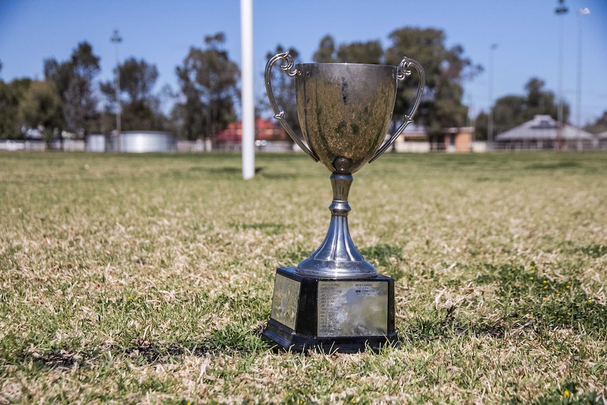 A silver trophy in front of goal posts at a football field.