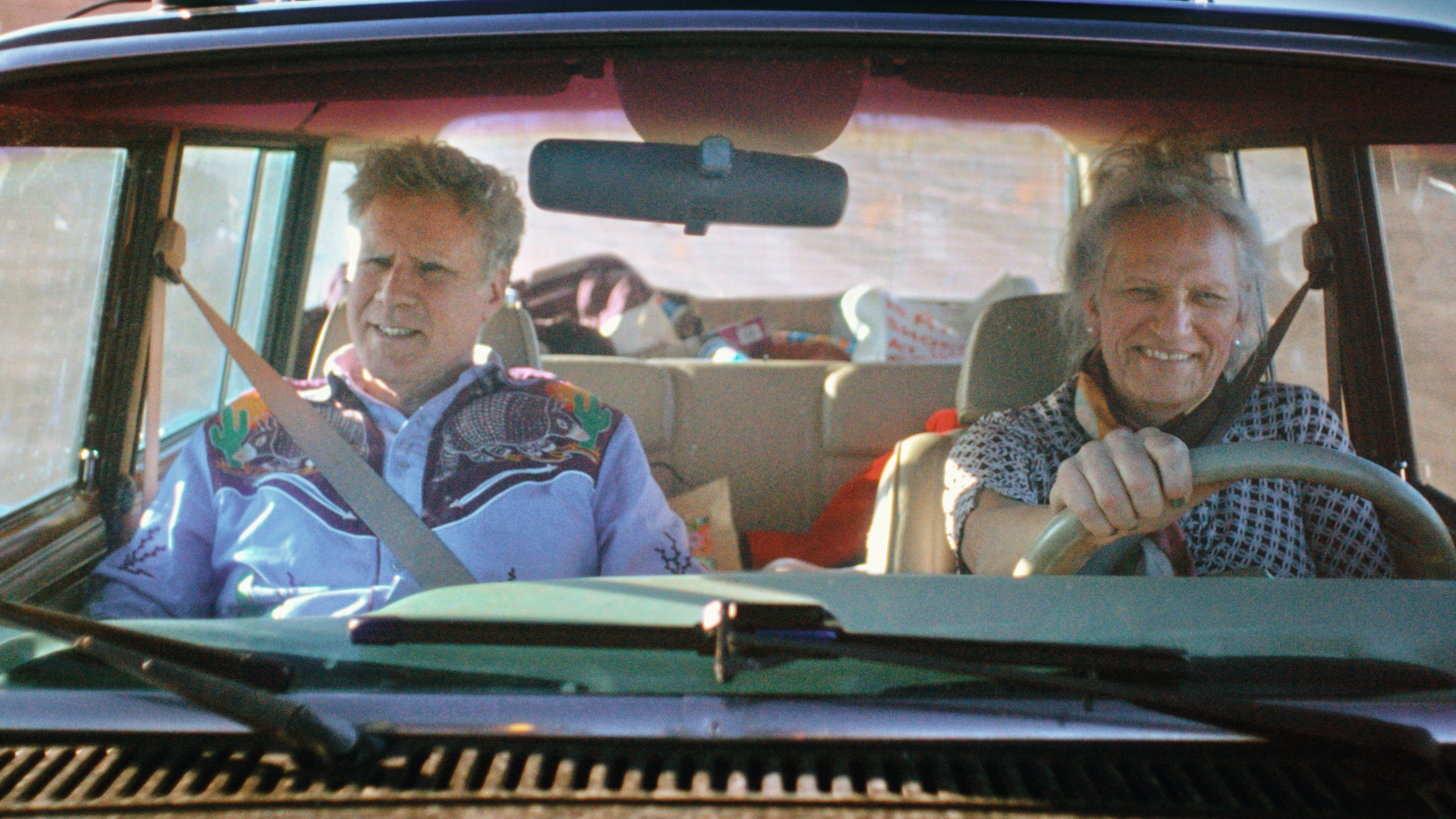 Will and Harper in a car, the image shot from the dashboard. They are on a bright road, both smiling.