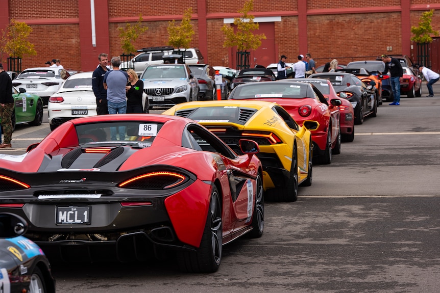 A line of sportscars amidst a carpark of other cars.