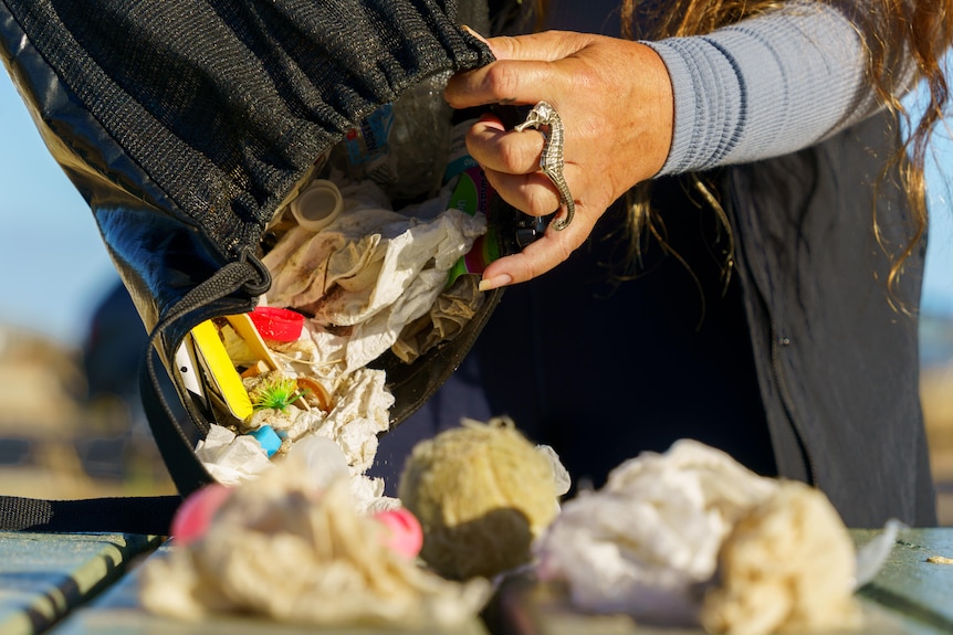 A woman with a seahorse ring pouring a bag of rubbish onto a table. 