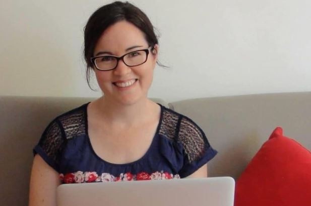 A woman wearing glasses sits with a laptop on her lap.