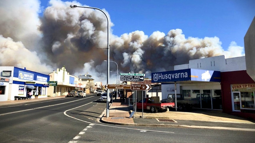 A rural town CBD with dark, billowing smoke behind.