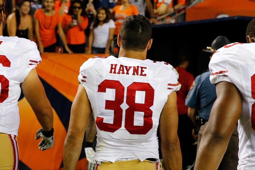 View from behind of Jarryd Hayne in his San Francisco 49ers number 38 jersey walking off the field with crowd in the distance.