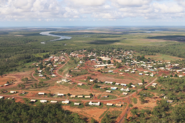 An aerial shot shows Wadeye community in the NT. There are large and small buildings spread out across dirt roads