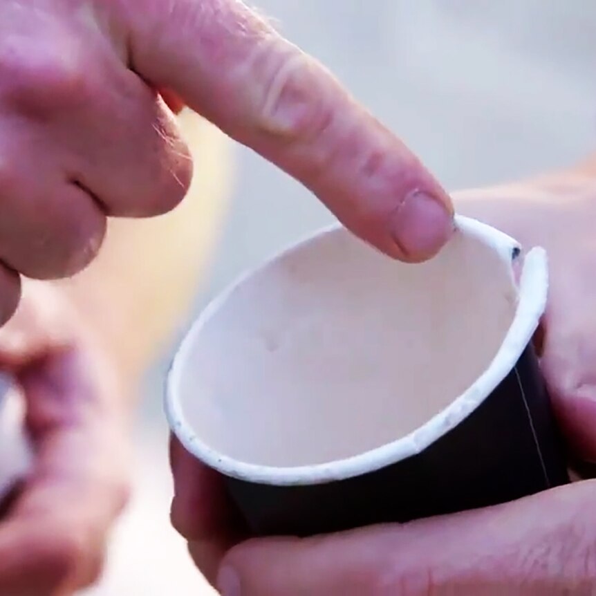 Hands hold an empty disposable coffee cup, fingers of another hand point to it
