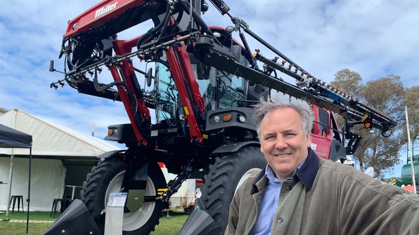 A man stands in front of a large piece of farm machinery.