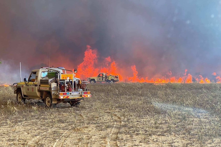 Two fire trucks pictured on an intense fire front with red flames right in front of one of the trucks