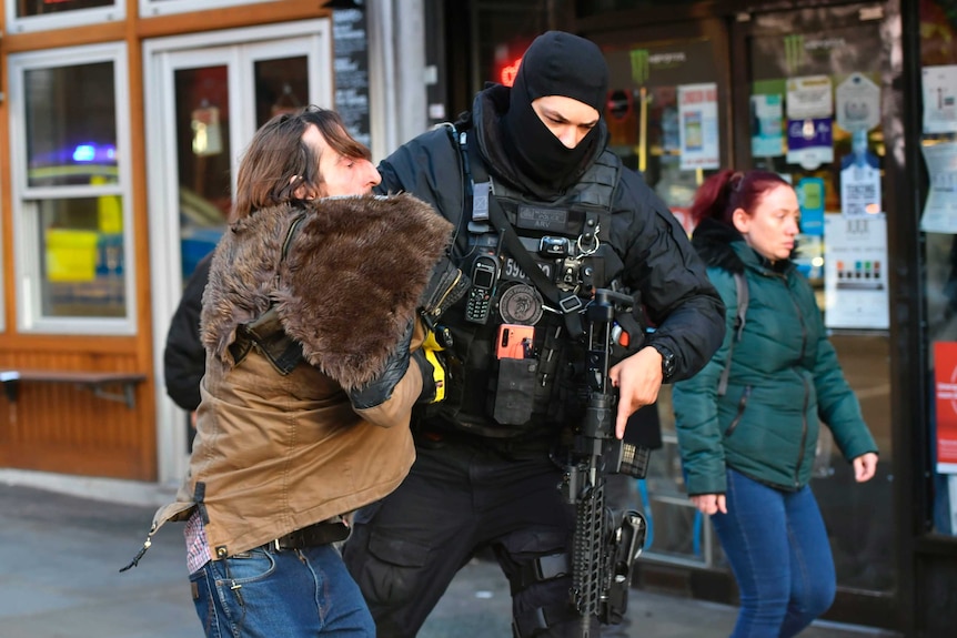 a police officer in a balaclava holds a gun in one hand while holding a man