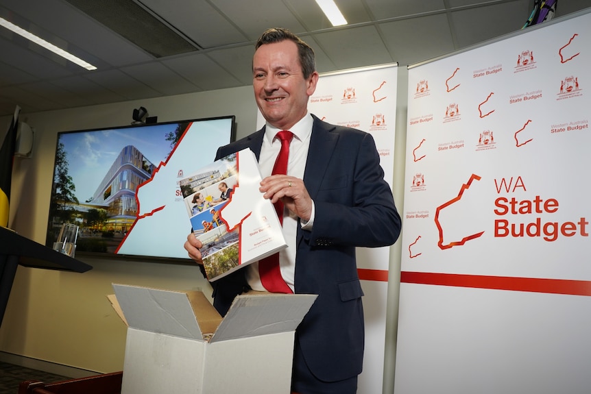 A man in a suit jacket and red tie holds up a document