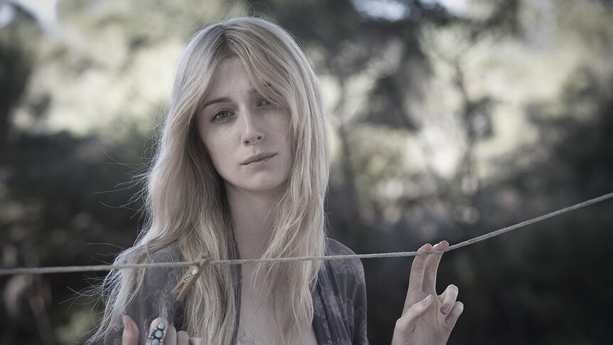Faded colour mid-shot photograph of actor Elizabeth Debicki standing in front of a clothes line in a backyard on a cloudy day.