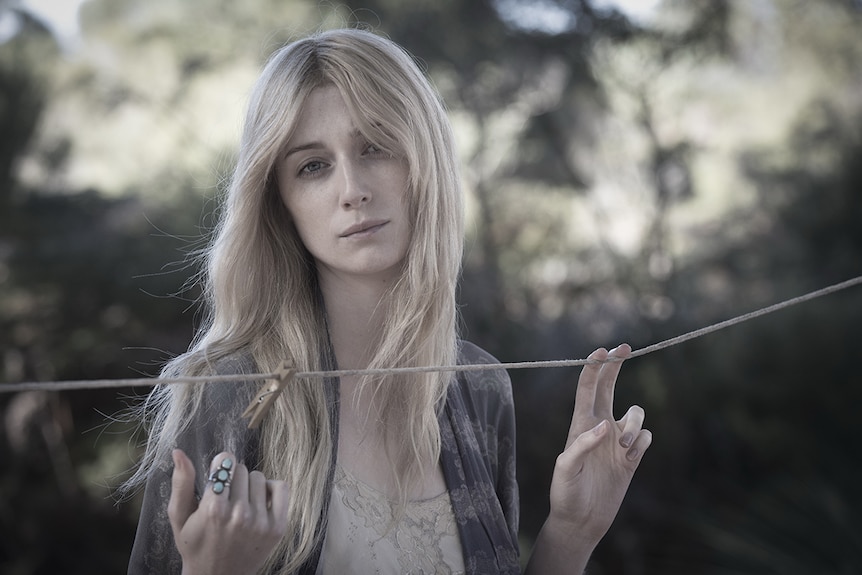 Faded colour mid-shot photograph of actor Elizabeth Debicki standing in front of a clothes line in a backyard on a cloudy day.