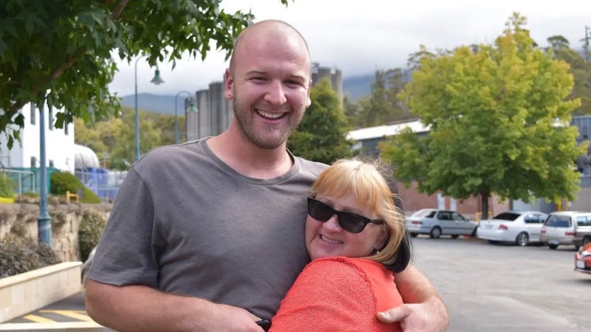 A tall smiling man puts his arm round a shorter woman who leans against him grinning. 