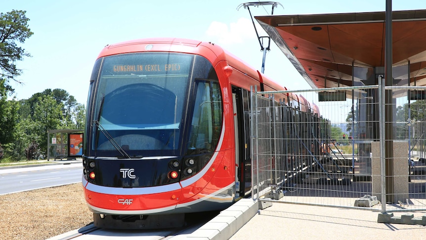 A bright light rail vehicle sits at a station still in the final stages of construction.