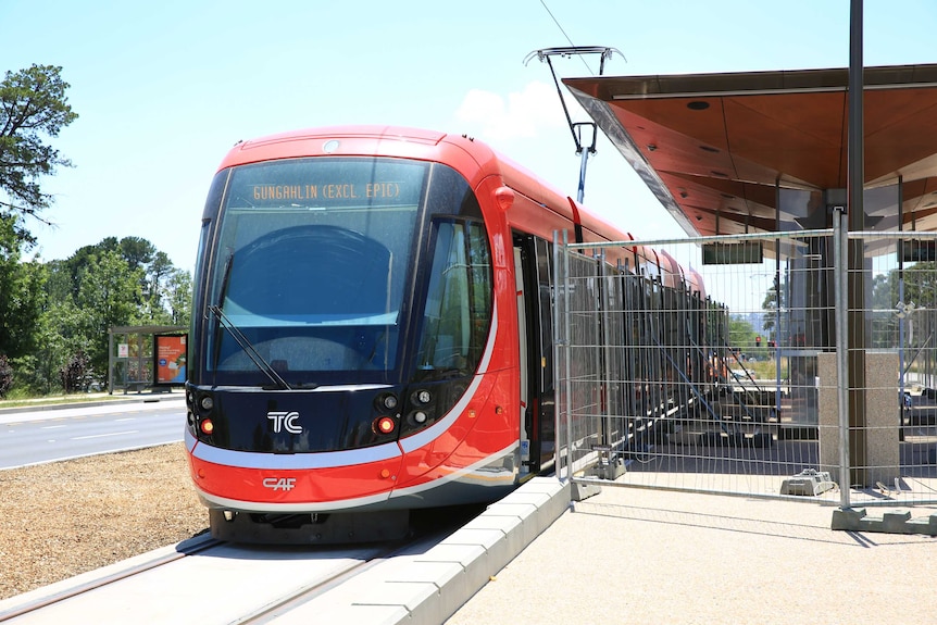 A bright light rail vehicle sits at a station still in the final stages of construction.