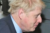 Boris Johnson walks towards a door to enter a meeting, avoiding the media camera taking pictures of him