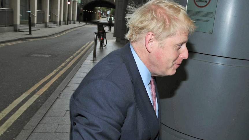 Boris Johnson walks towards a door to enter a meeting, avoiding the media camera taking pictures of him