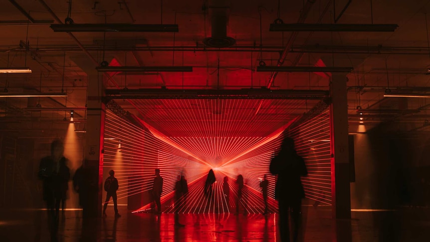 An art installation at Dark Mofo shows many red lasers shooting in a pattern as people walk through it.
