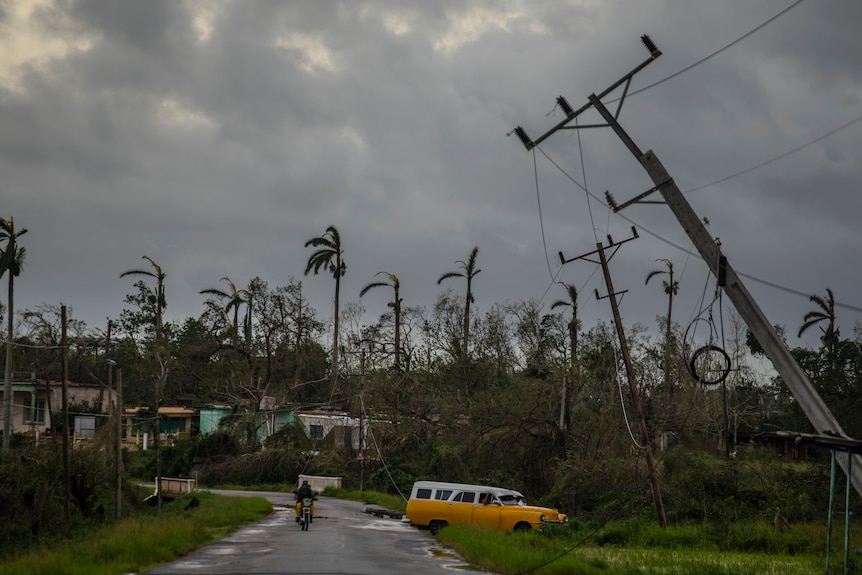 A man is riding a bicycle down  a road with fallen powerlines alongside it. 