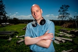 Haydn Payne, a bald headed man with a blue shirt, with his noise cancelling headphones around his neck.