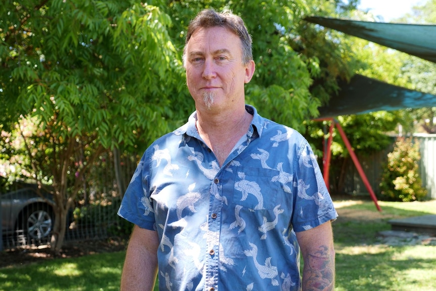 A man standing in a grassed area with play equipment.