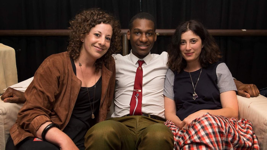 Three people are seated on a couch.