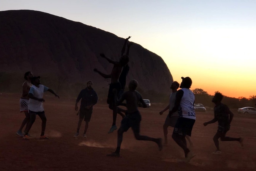 Silhouettes of people playing footy