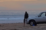 A man sits on the bonnet of a car watching the sunset on Aldinga Beach.