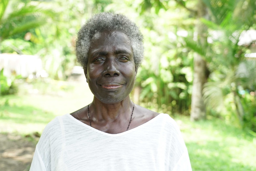 Magdalene Toroansi smiles and stares at the camera in front of bright background of trees.