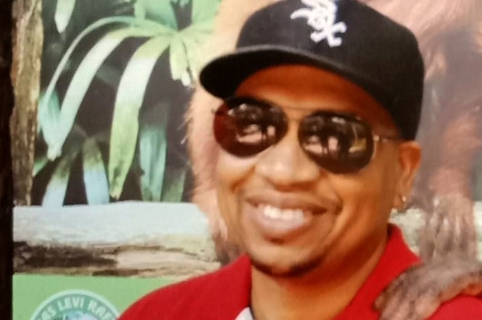 A mid shot of Harold Carter smiling and posing for a photo wearing a black baseball cap and red polo shirt.