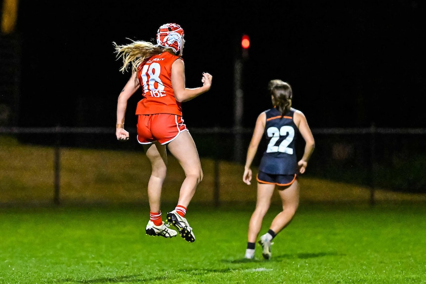 A woman in red and white headgear jumps and clenches her fist on a football field.