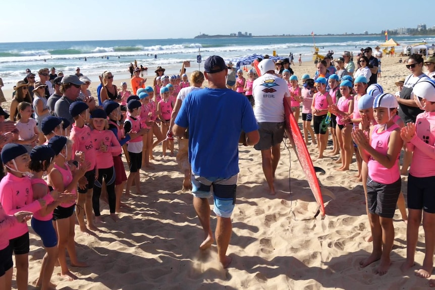Children in pink vests form a guard of honour on the beach and applaud a family walking through.