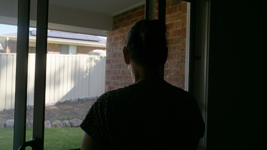 A woman stares out of the glass door at the back of her house.
