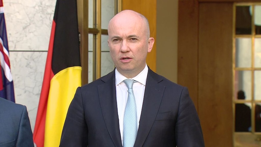Man in suit and tie speaking at a media conference at Parliament House.