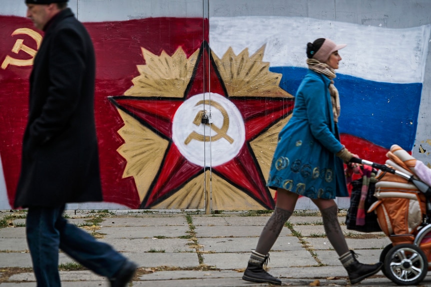 People pass by the Soviet Union's flag on a mural in Luhansk