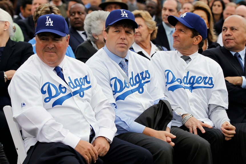 Los Angeles Dodgers co-owners Robert L Patton Jr, Todd Boehly, and Peter Gruber sitting wearing Dodgers hats and jerseys