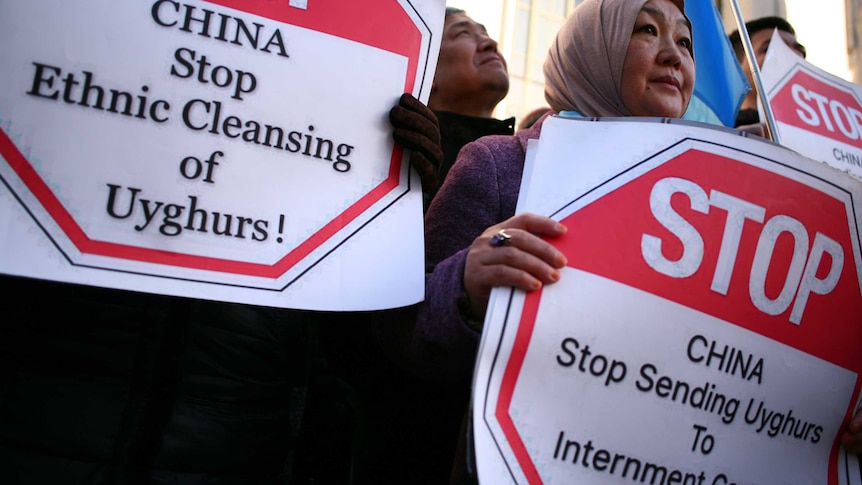 Ollder woman with headscarf holds a placard saying China stop sending Uyghurs to internment camps