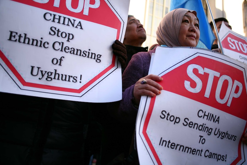Ollder woman with headscarf holds a placard saying China stop sending Uyghurs to internment camps