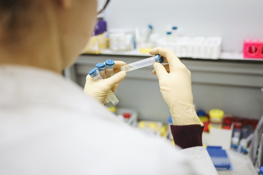 A woman in a white lab coat holds several test tubes