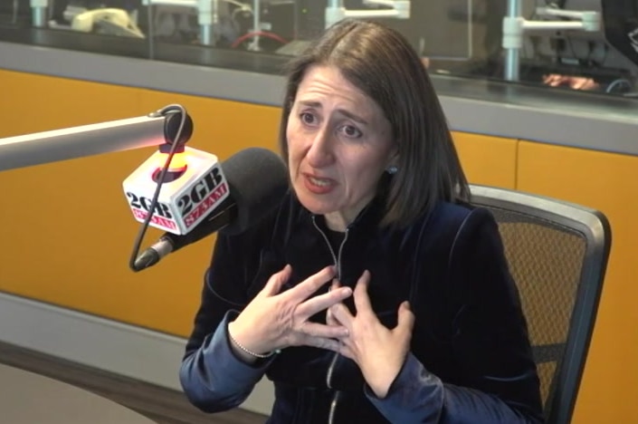 Ms Berejiklian is gesturing to herself and sitting behind a microphone with a 2GB logo on it.