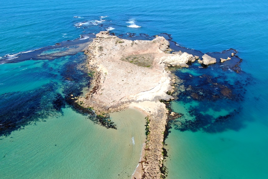 A drone shot of a sea wall extending to a point of land with the ocean surrounding it.