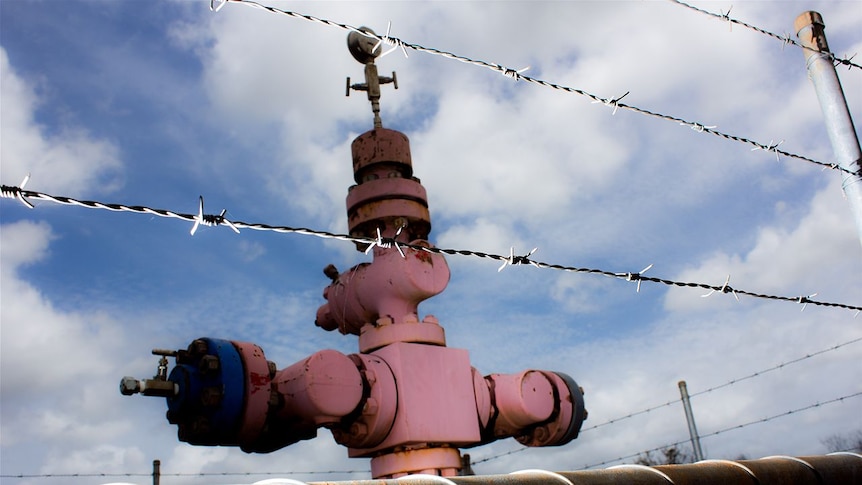 A wellhead behind a barbed wire fence.