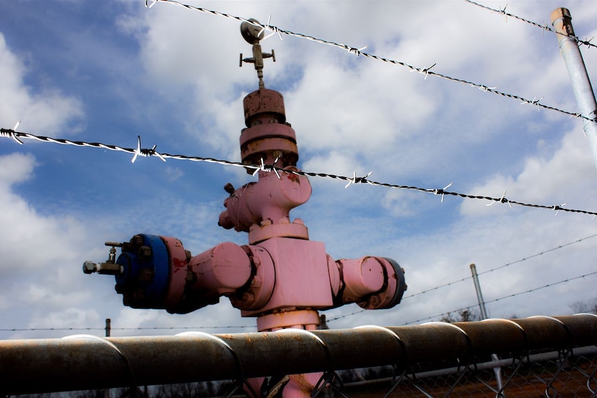 A wellhead behind a barbed wire fence.