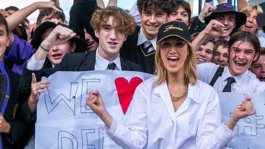 An image of Delta Goodrem with students behind her holding signs