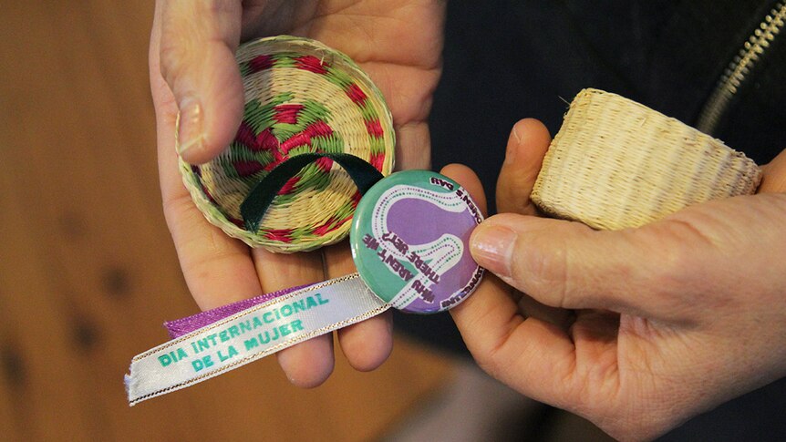 Woman holds a purple badge in her hands that says 'international women's day' in spanish.