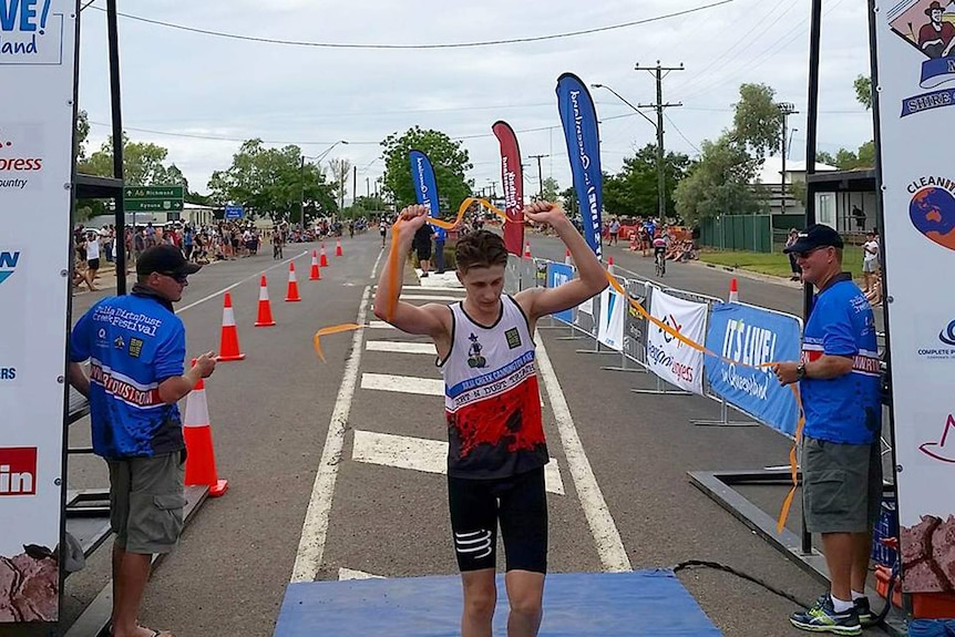 A man runs through the tape at the end of a triathlon