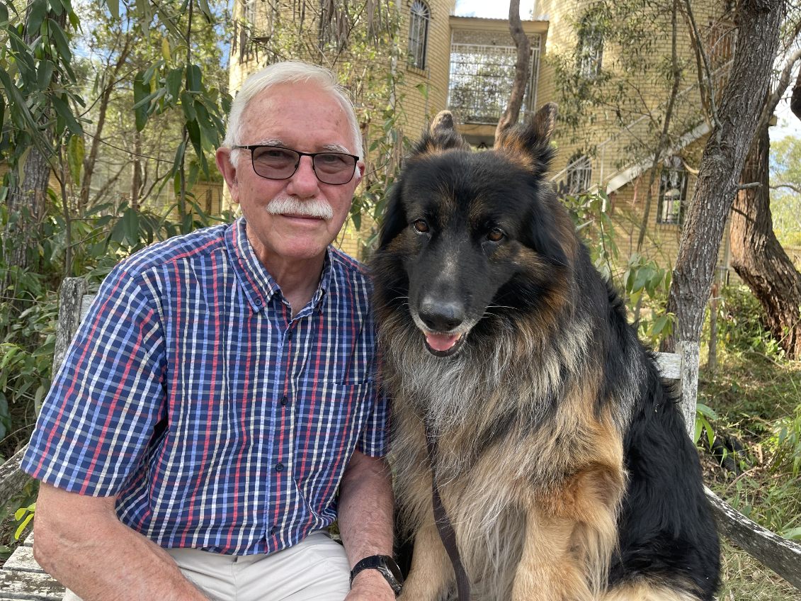Dr Day sits with his large dog in front of a tree. He is smiling.
