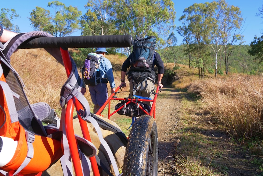 A person pulls a cart through the countryside with another person at their side.