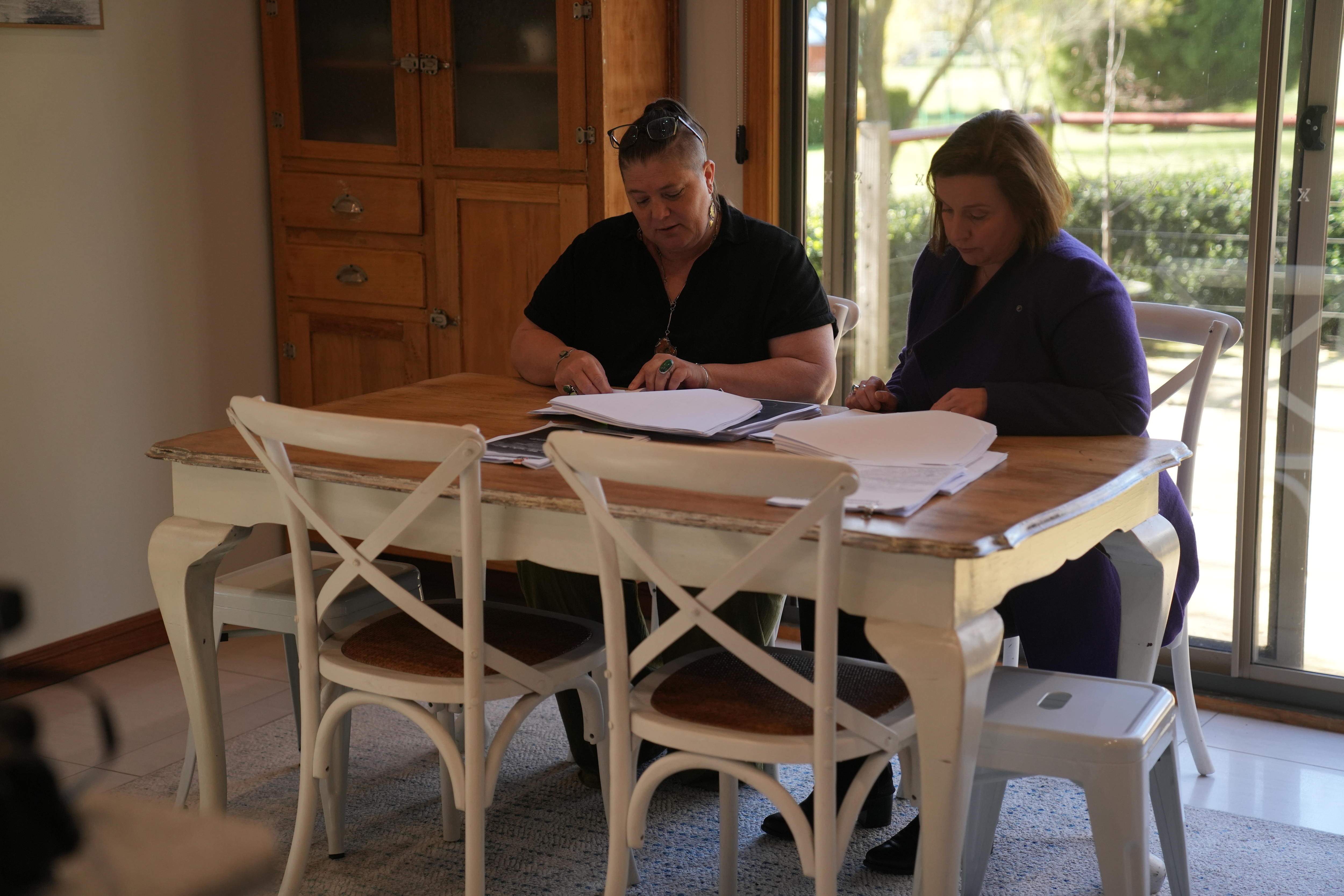 The pair sit inside, looking at piles of documents on the table.