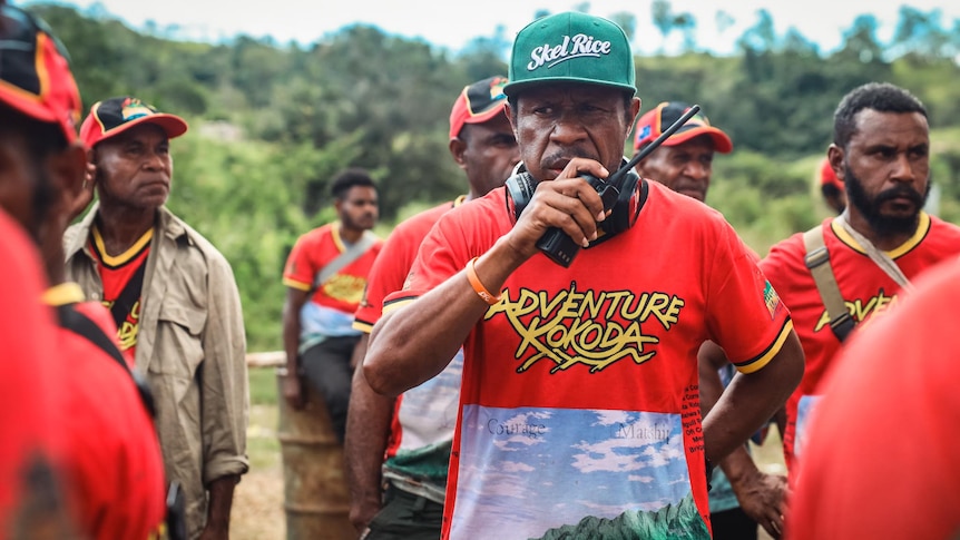 A man in a red Adventure Kokoda t-shirt speaking into a walkie talkie